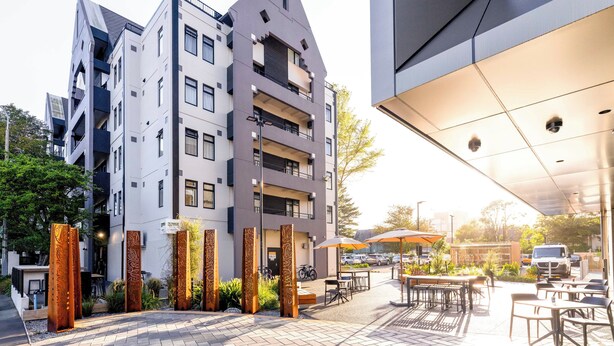 A modern building with multiple floors, outdoor seating area, and decorative metal panels. - Hotel Give (Christchurch)