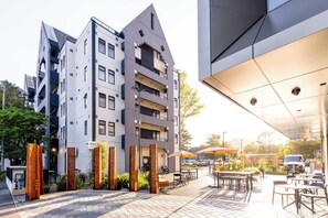 Un bâtiment moderne à plusieurs étages, doté d’un espace extérieur aménagé pour s’asseoir et de panneaux métalliques décoratifs.
