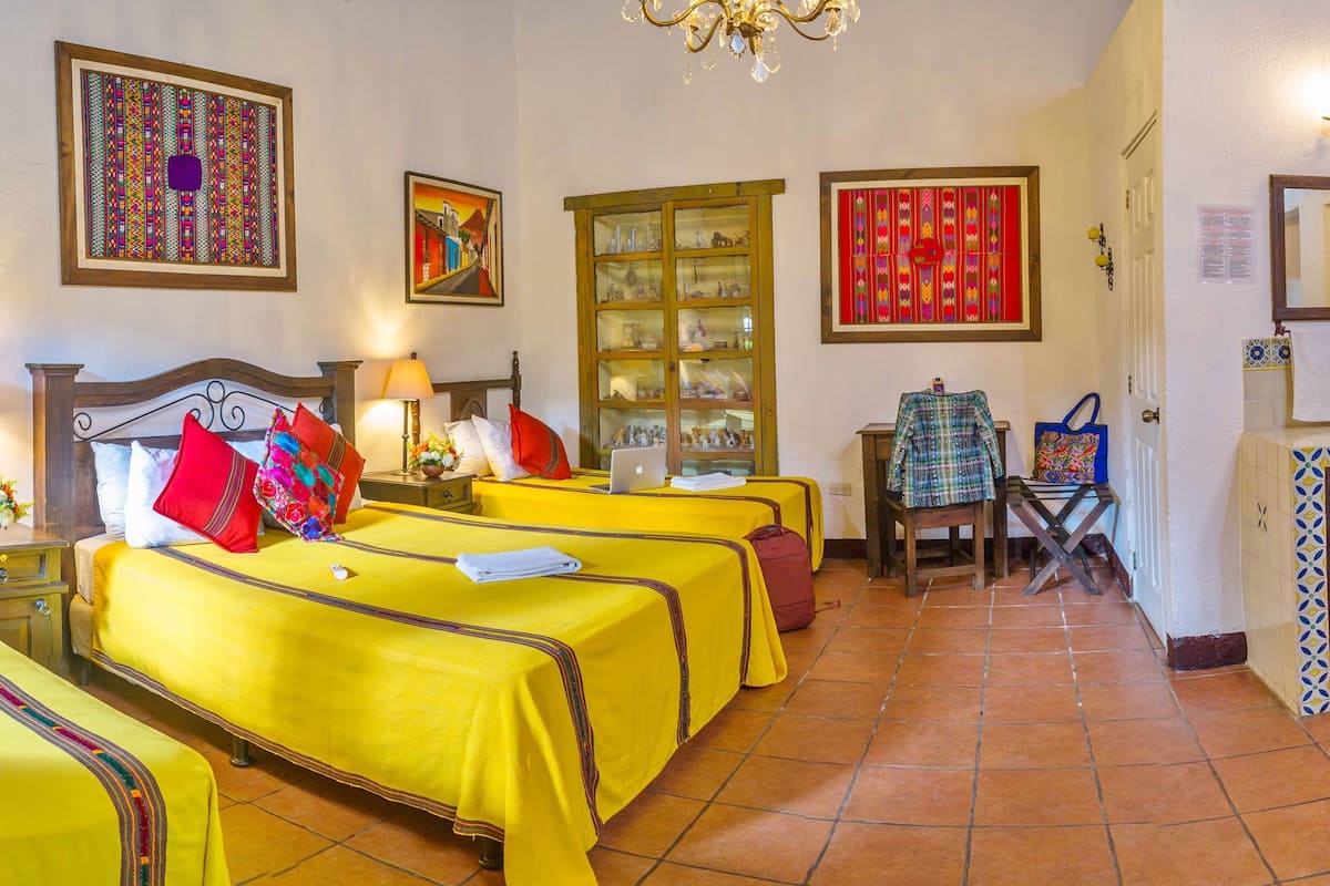 A hotel room with four beds, a desk with a chair, a mirror, and a cabinet with glass doors.