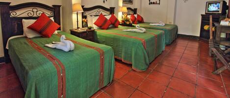 Habitación de hotel con tres camas, cada una con cubrecama verde y almohadas rojas, un candelabro y un televisor sobre un soporte de madera.