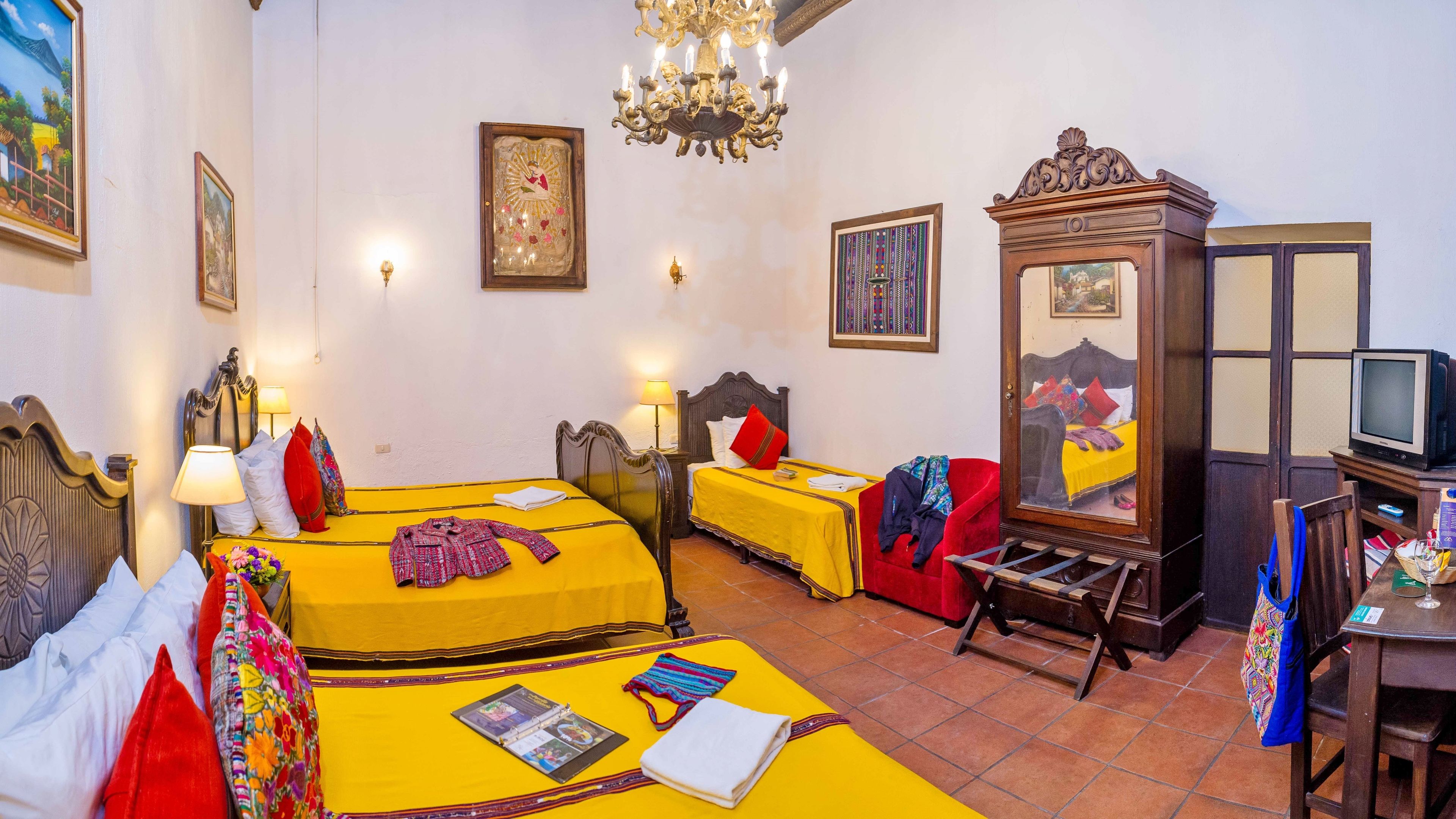 A hotel room with two beds, a television, a mirror, and a chandelier.