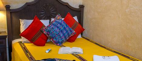 A neatly made bed with a yellow bedspread, red and multicolored pillows, and a book and remote control on it.