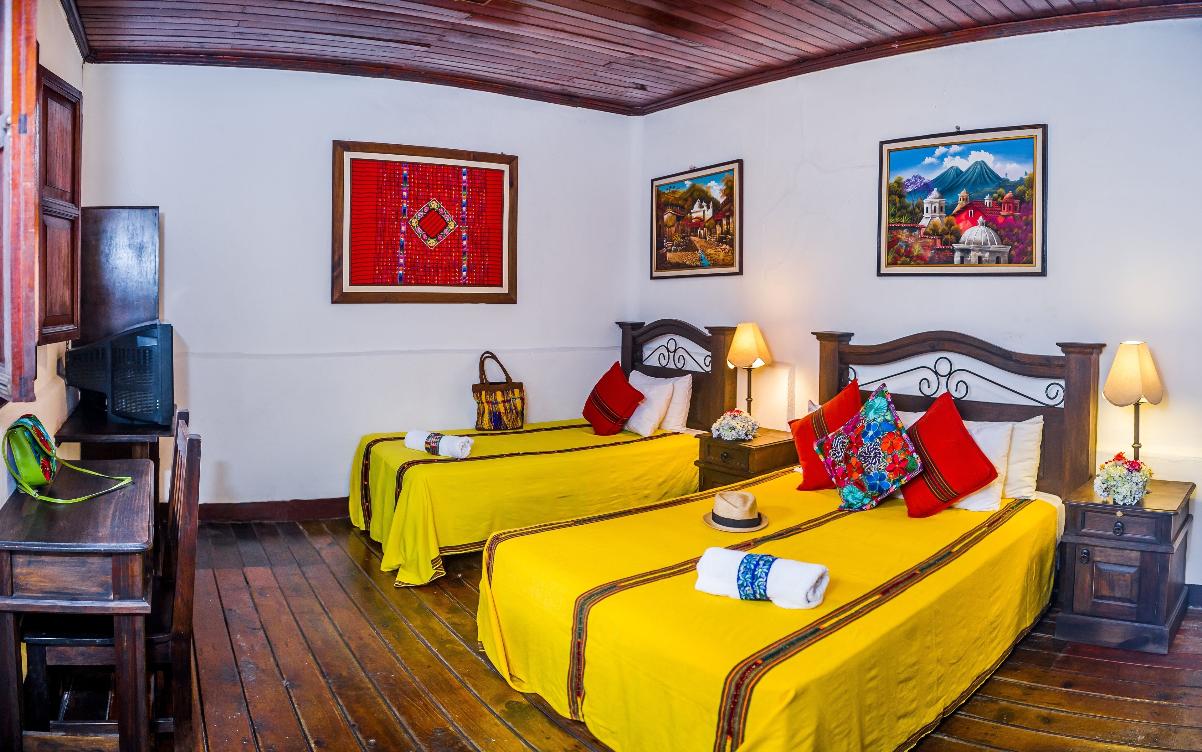 A hotel room with two beds, wooden flooring, a television, and artwork on the walls.
