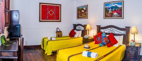 A hotel room with two beds, wooden flooring, a television, and artwork on the walls.