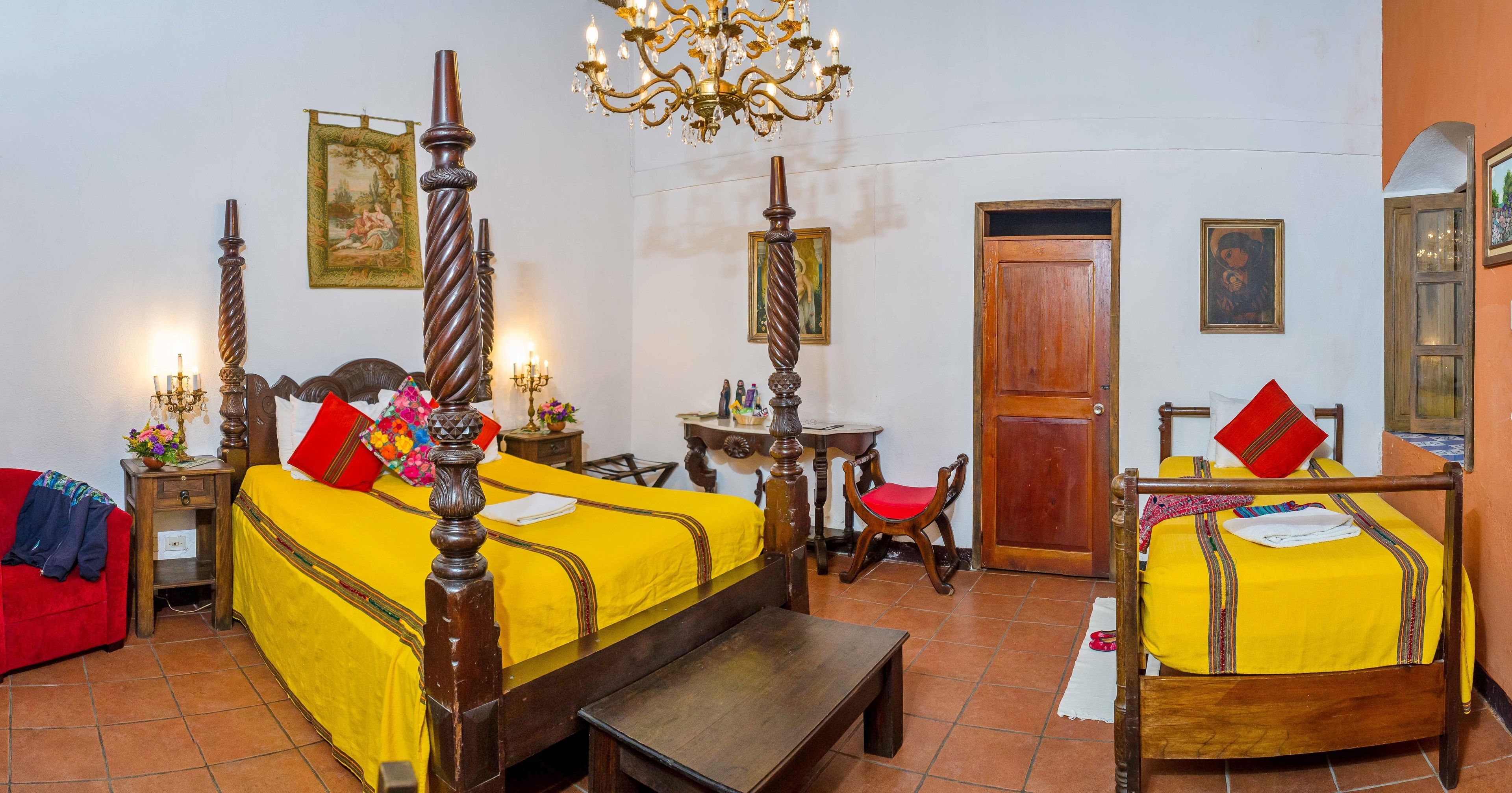 A room with a large bed, a wooden chair, a small table, and a chandelier.