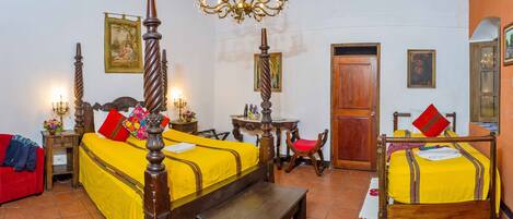 A room with a large bed, a wooden chair, a small table, and a chandelier.