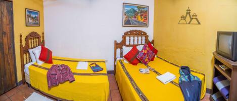Habitación con dos camas, cada una con colcha y almohadas amarillas, cabeceros de madera, un televisor y una pared con dos cuadros enmarcados.