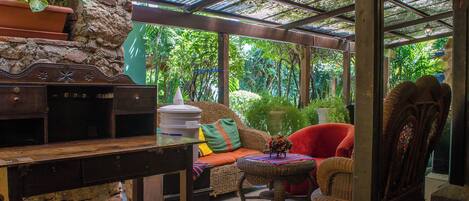 A cozy outdoor seating area with a stone wall, a wooden table, and wicker furniture.