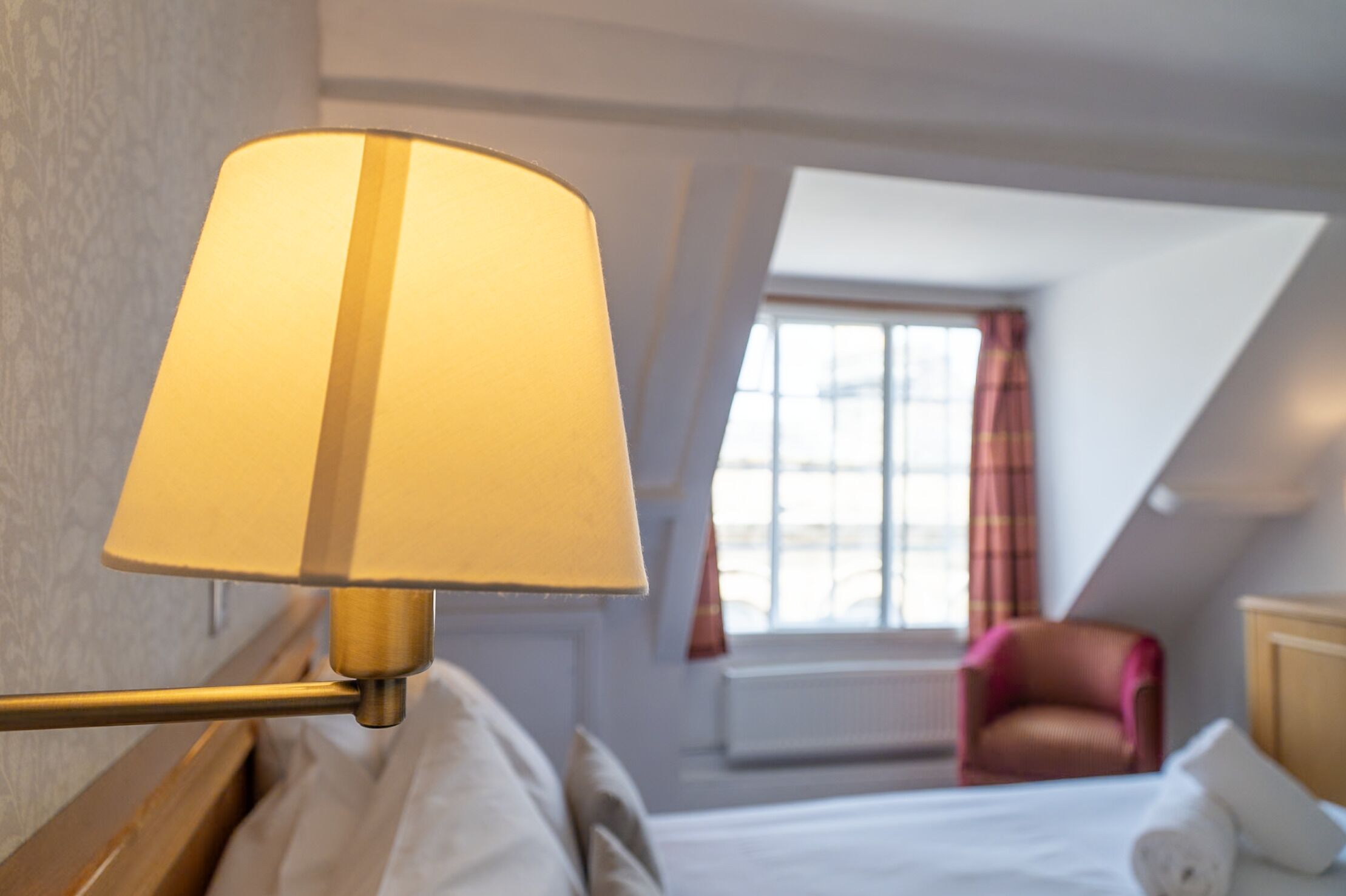 A hotel room with a bed, a lamp, a chair, and a window with curtains.