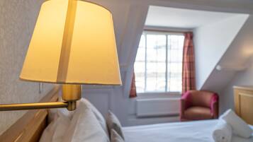 A hotel room with a bed, a lamp, a chair, and a window with curtains.