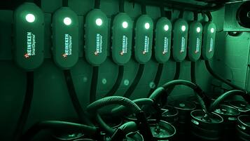 A row of HEINEKEN SmartDispense machines with hoses and kettles in a dimly lit room.
