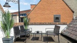 A rooftop patio with two black metal chairs and a small table, surrounded by potted plants.