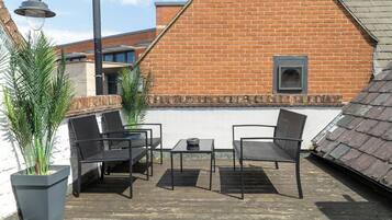 Une terrasse sur le toit, avec deux chaises en métal noir et une petite table, entourée de plantes en pot.