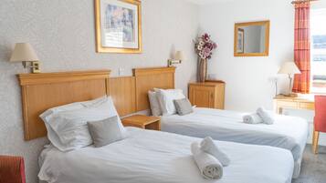 A hotel room with two beds, a wooden headboard, a framed picture, a vase with flowers, a mirror, and a red chair.