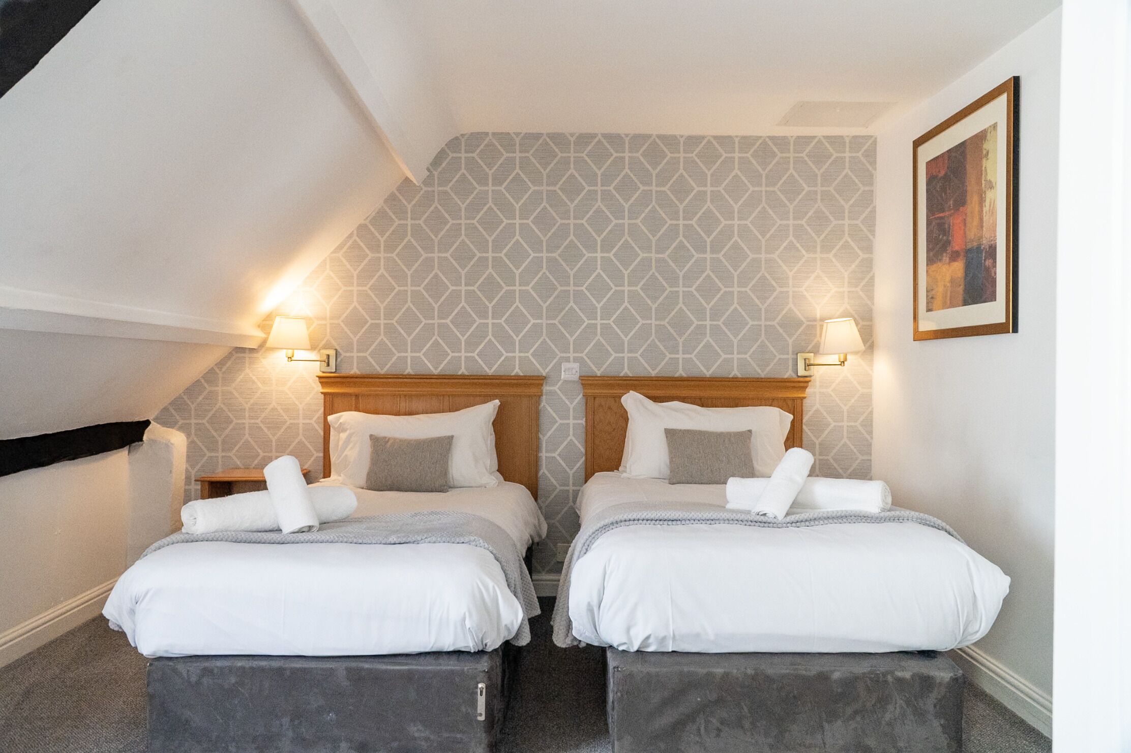 Habitación doble con dos camas, cada una con cabecera, lámparas de noche y un cuadro en la pared.