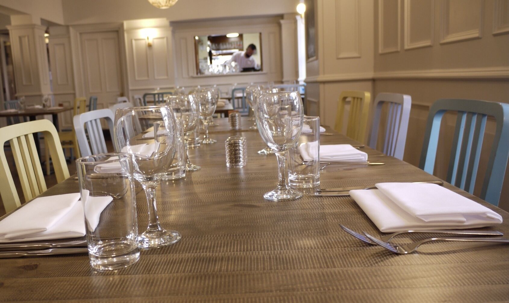 A dining table set with multiple wine glasses, napkins, and cutlery, with chairs around it.