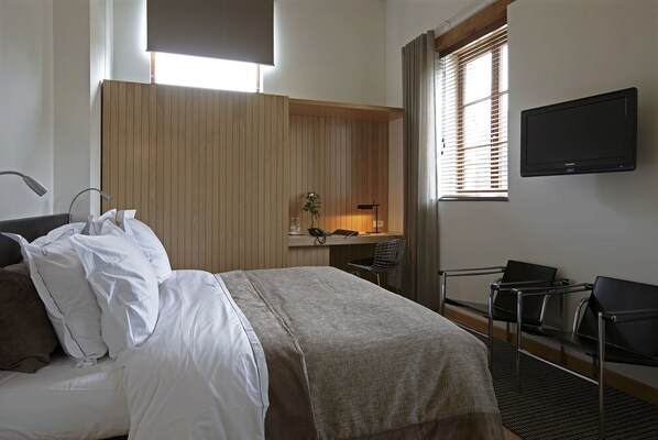 A hotel room with a bed, a desk, a chair, and a television.