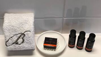 Une salle de bain avec une serviette blanche, un savon en barre et trois flacons de savon liquide posés sur le lavabo.