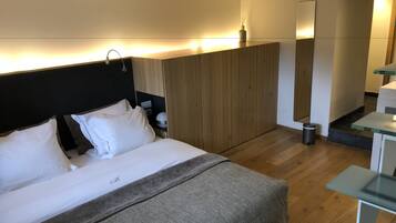 Een hotelkamer met een bed, nachtkastje, lamp en een houten garderobe.