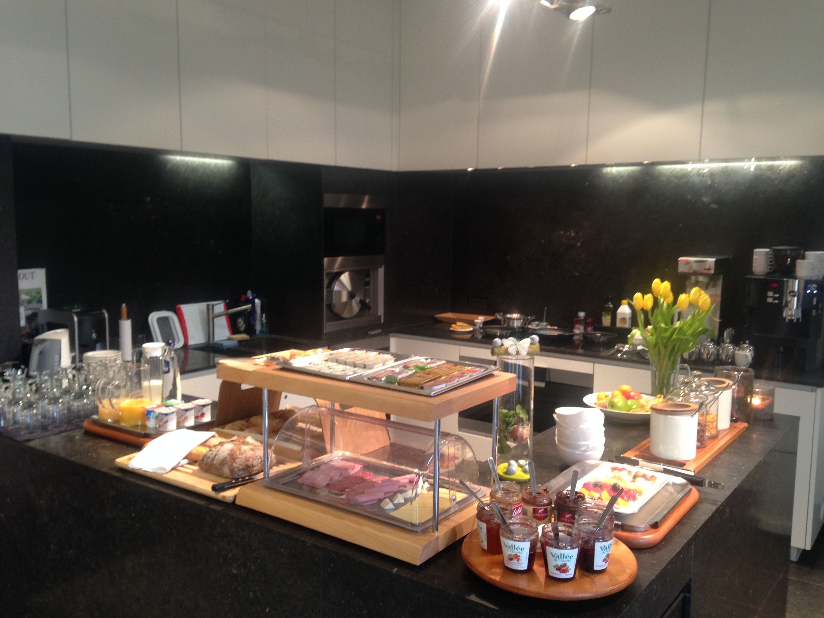 A buffet setup with various food items, a coffee station, and a vase of yellow tulips.