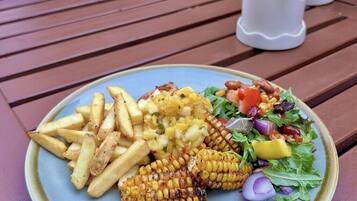 A plate with fries, grilled corn, and a salad on a wooden table.