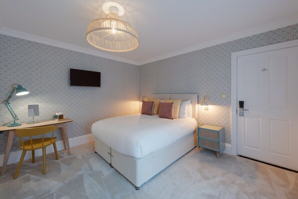 A bedroom with a bed, desk, chair, nightstand, and a door.
