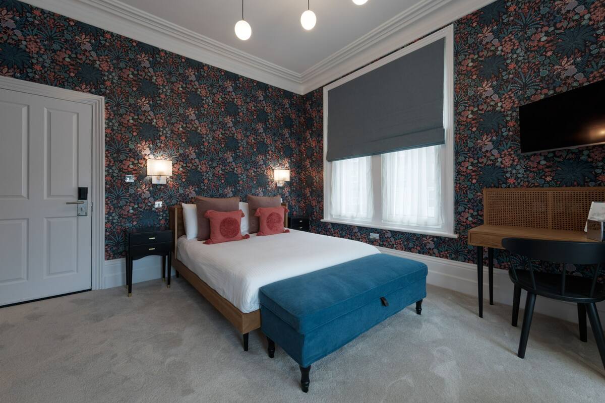 A bedroom with a bed, bedside tables, a desk, and a window with a blind.