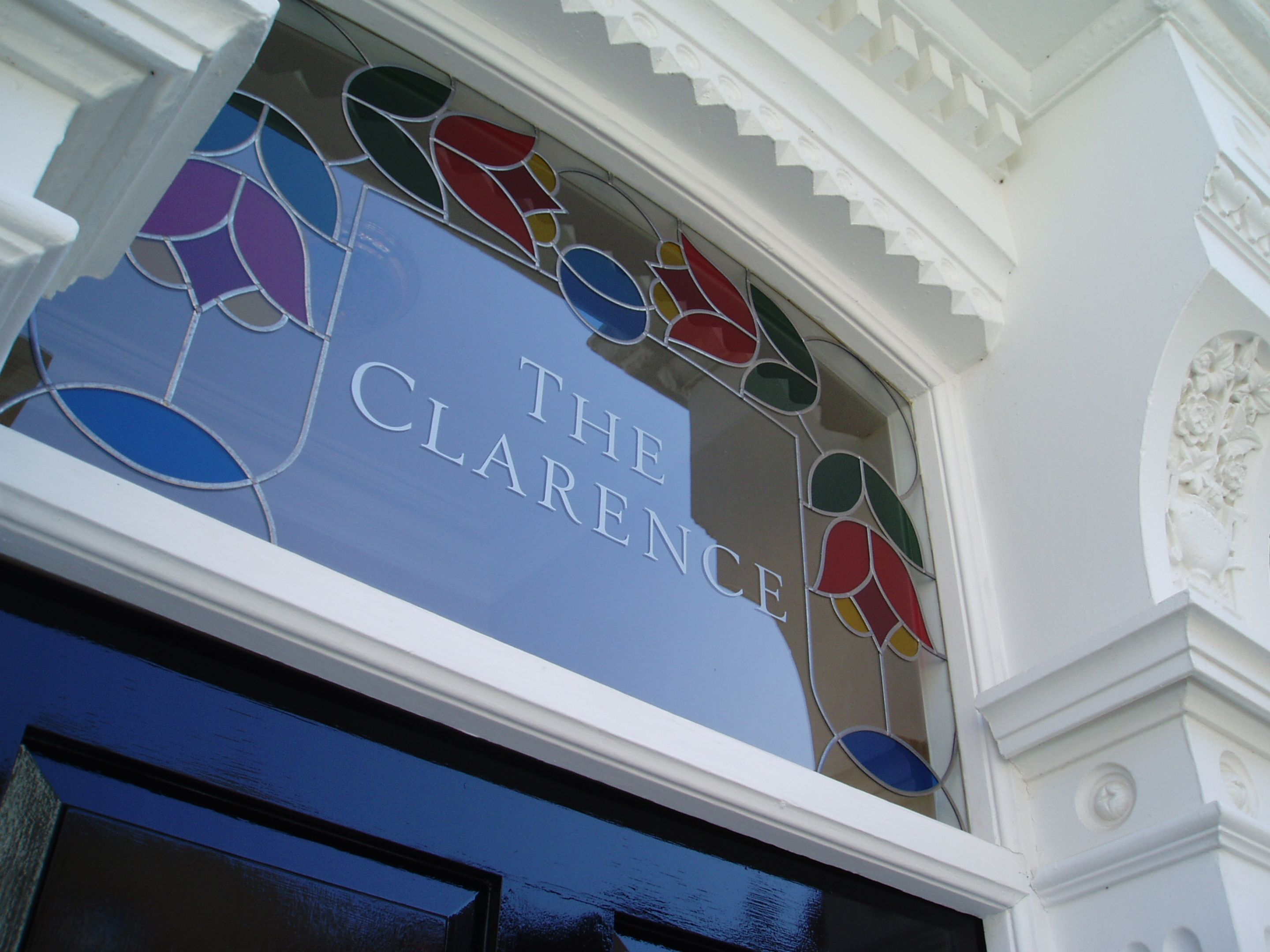 A stained glass window with the inscription "THE CLARENCE" on a blue background.