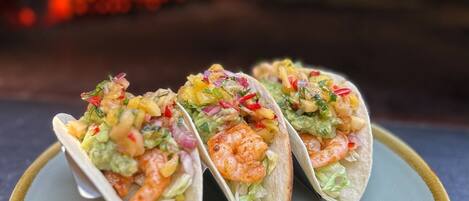 Three tacos on a plate with a pizza oven in the background.