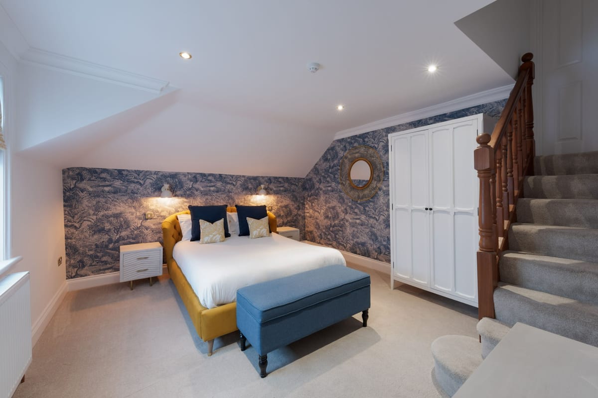 A bedroom with a bed, bedside tables, a bench, a wardrobe, and a staircase.