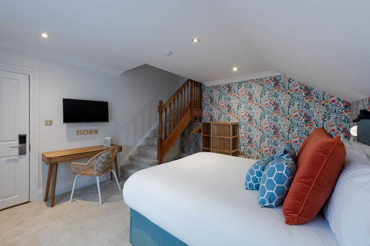 A bedroom with a bed, a desk, a chair, a TV, and a staircase.