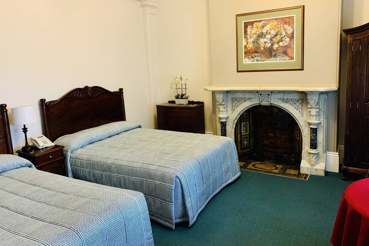 Una habitación de hotel con dos camas, chimenea, un cuadro y un teléfono sobre una mesita de noche.