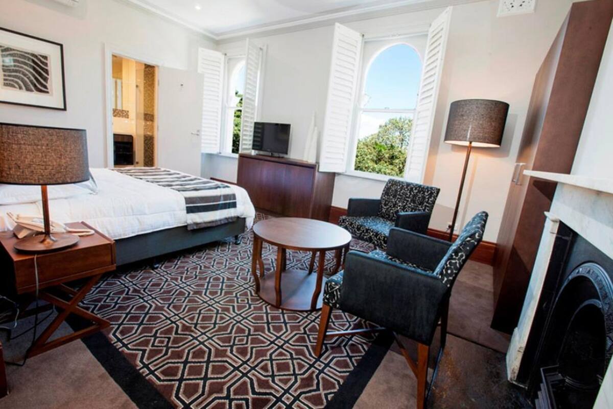Un dormitorio con cama, escritorio, silla, televisor, chimenea y alfombra estampada.