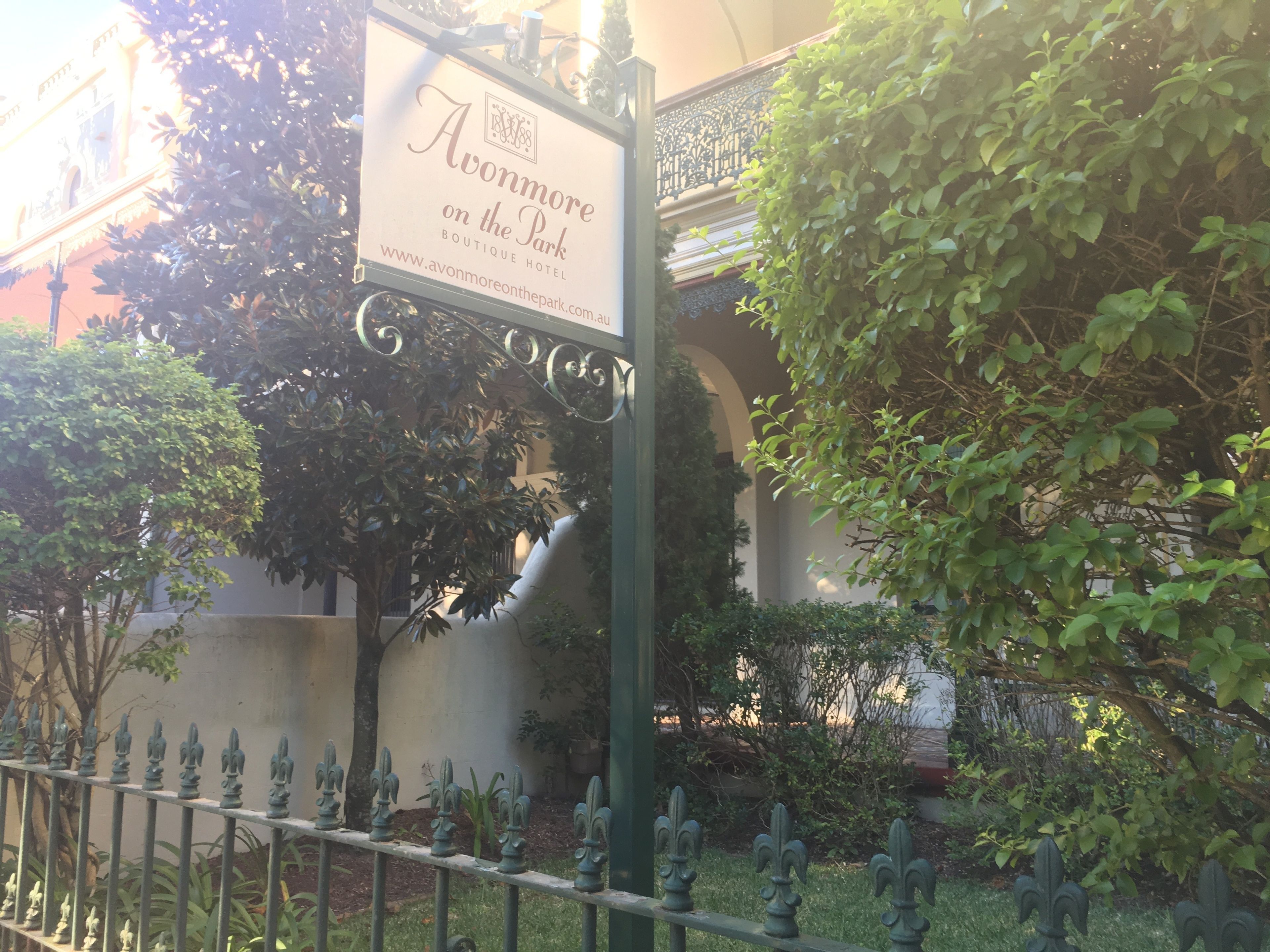 A sign for 'Avonmore on the Park Boutique Hotel' with a wrought iron fence and greenery in the background.