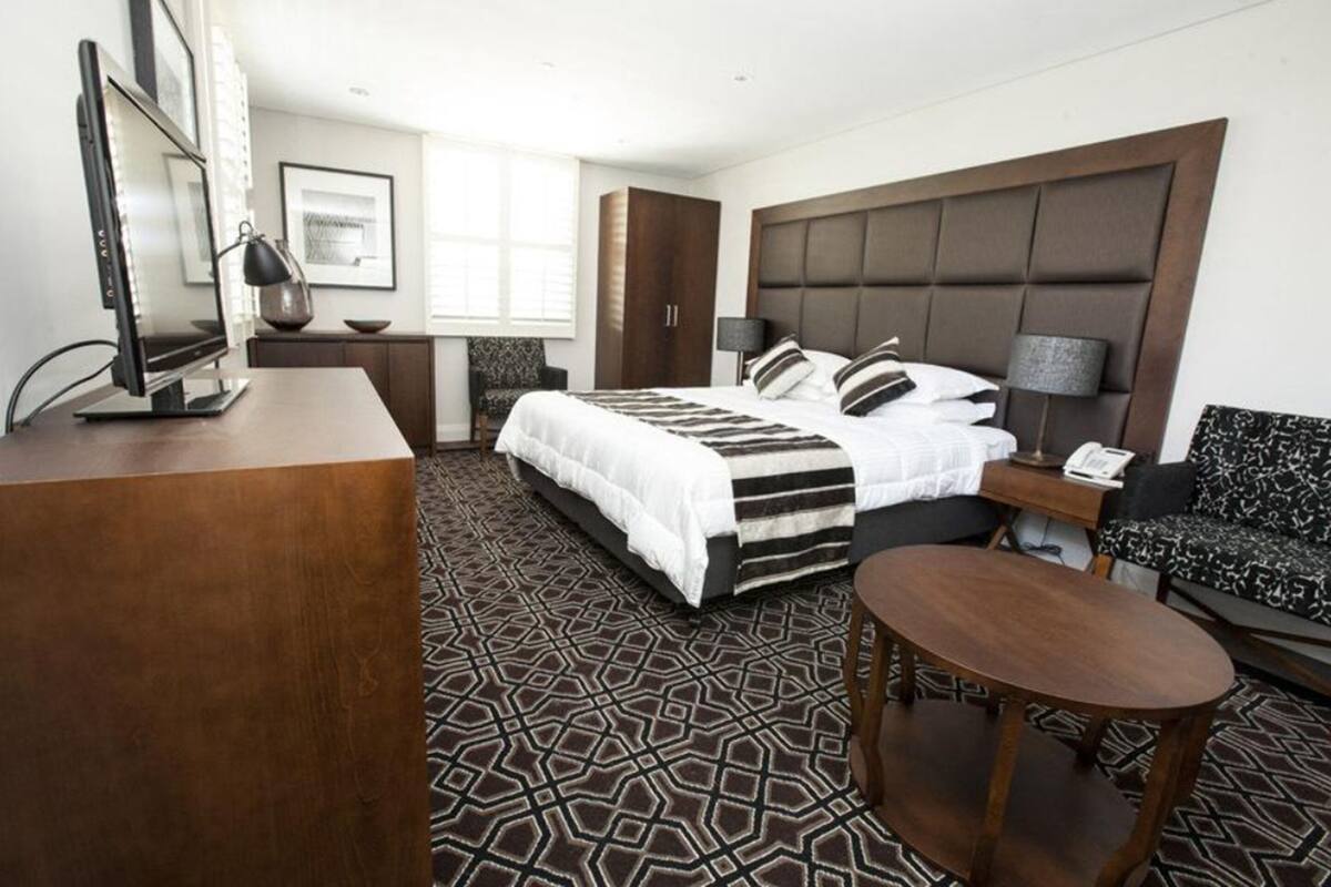 Una habitación de hotel con una cama grande, un escritorio, una silla, una mesita y un armario.