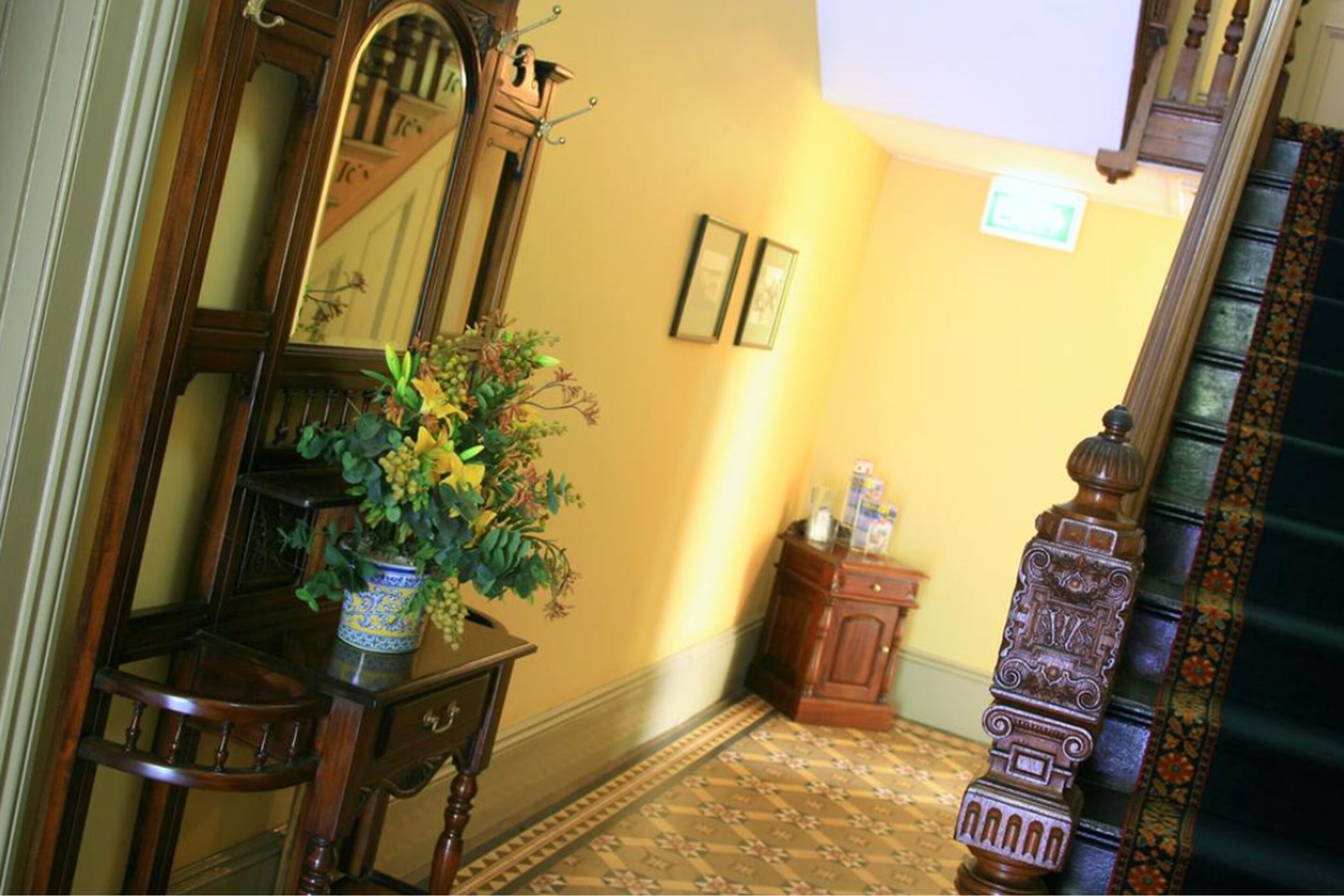 A hallway with a wooden chair, a blue vase with flowers, a mirror, and a wooden cabinet.