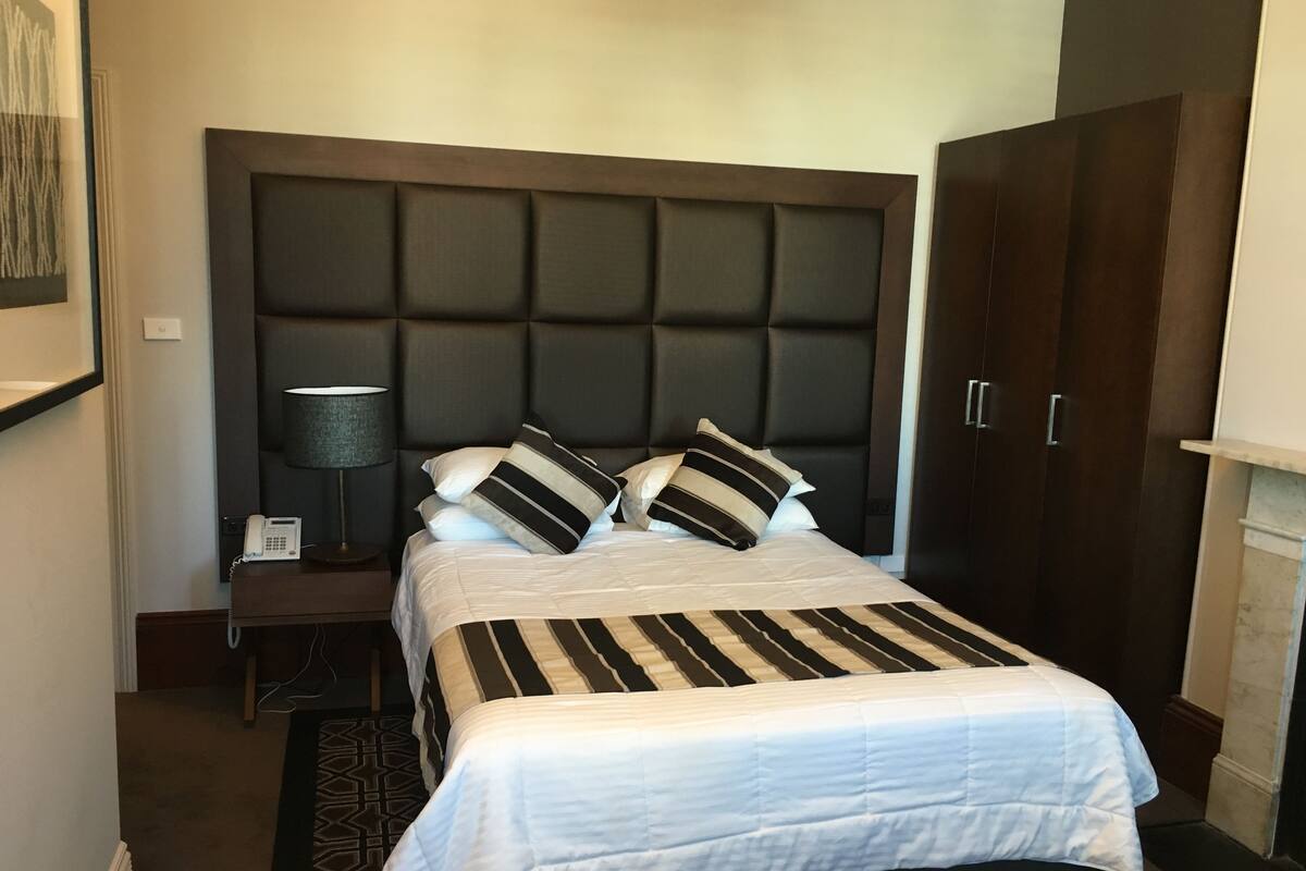 Una habitación de hotel con una cama grande, una mesita de noche con una lámpara, un teléfono y un armario.