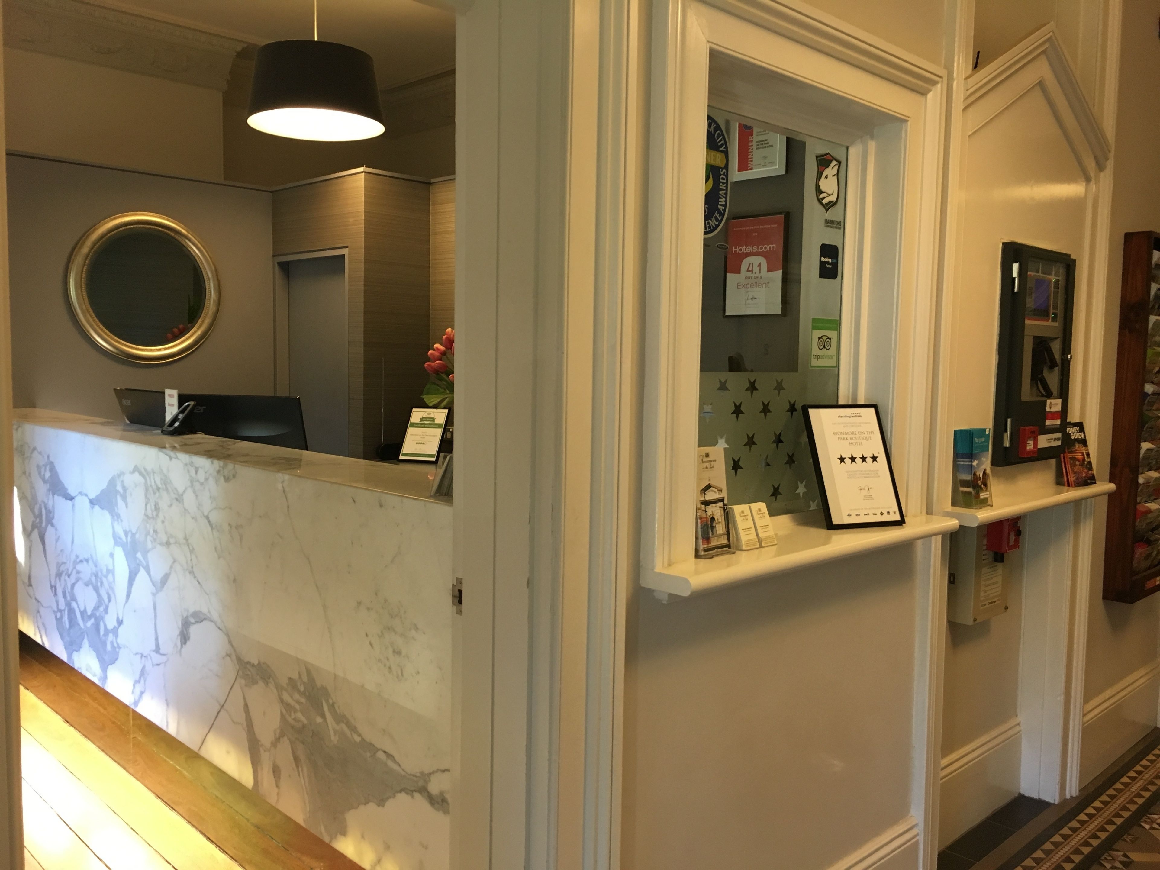 A hotel reception area with a marble counter, a round mirror, and a display of awards and certificates.