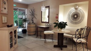 A reception area with a reception desk, a seating area with a sofa and chairs, a large potted plant, a decorative mirror, and a wall-mounted fan. - Le Mas du Colombier (Cadenet)