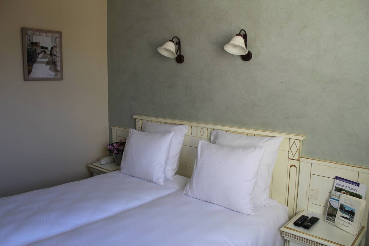 A hotel room with a bed, two bedside tables, a nightstand, a wall-mounted lamp, and a framed picture on the wall.