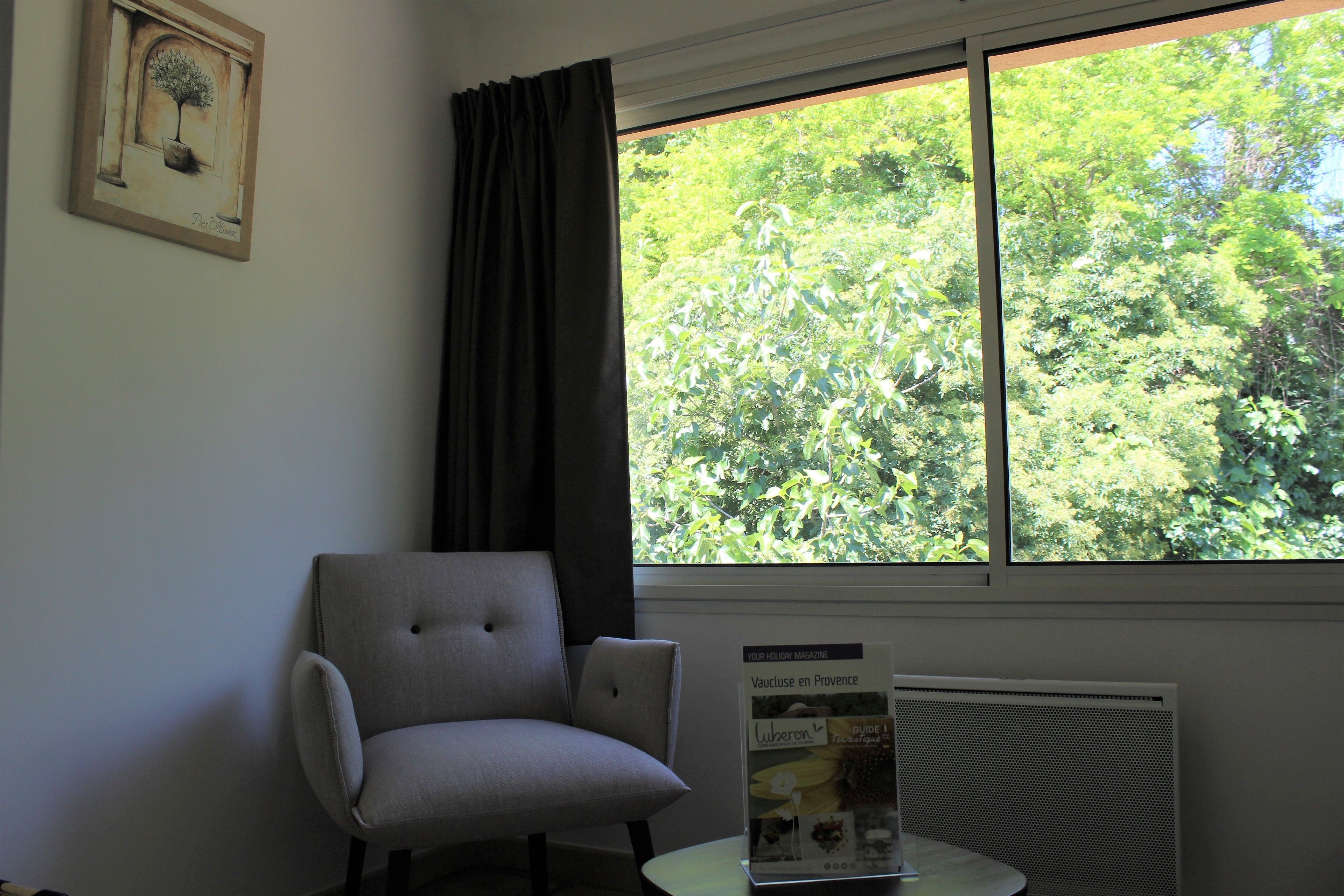 A room with a window, a chair, a radiator, and a framed picture on the wall.