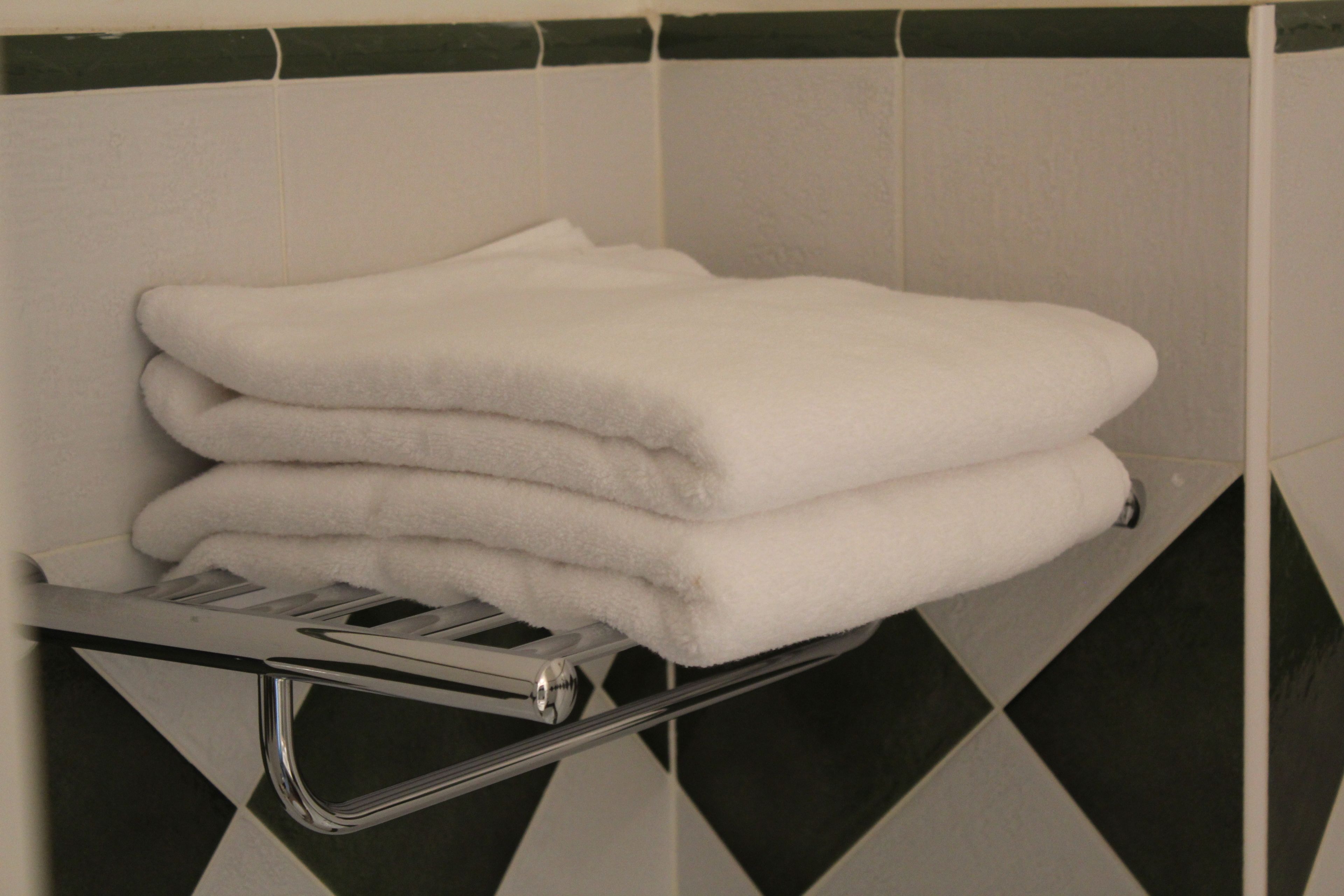 A stack of white towels on a chrome towel rack in a bathroom with black and white checkered tiles.