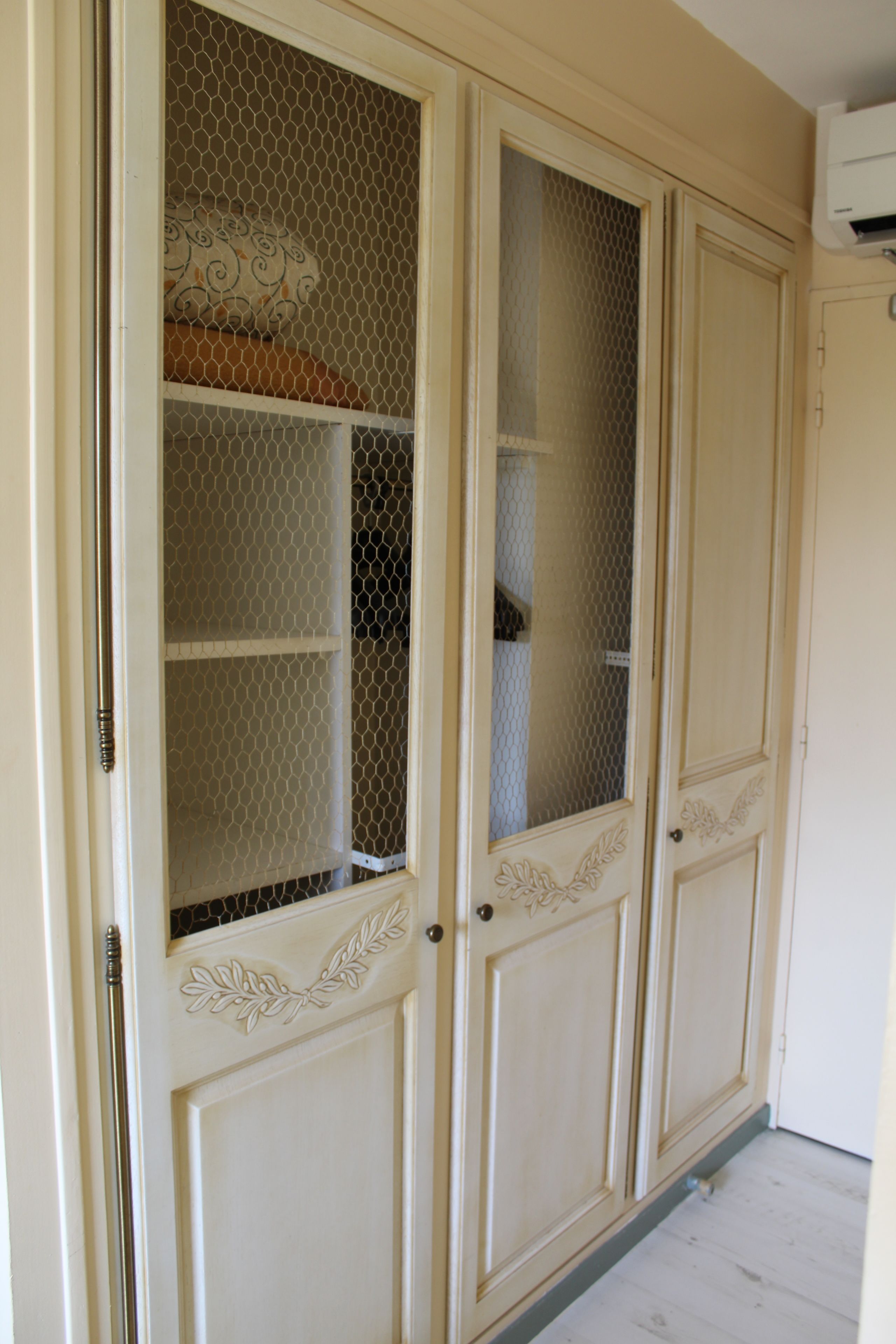 A room with a wardrobe featuring a mesh door and a decorative handle.