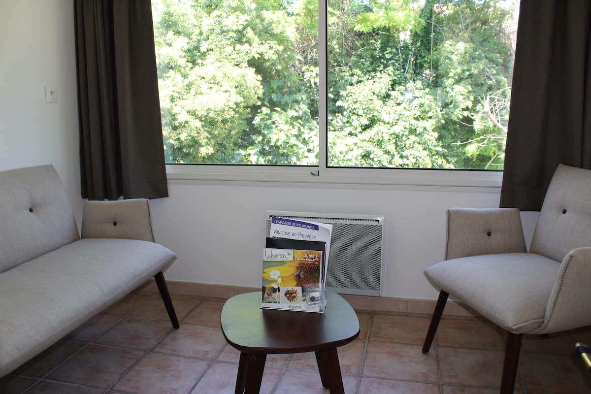 A room with two sofas, a small table with a magazine, and a window with a view of trees.