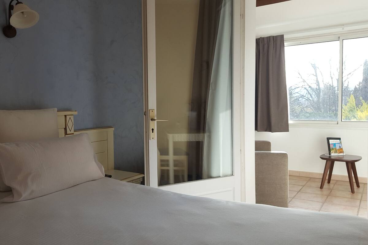 A bedroom with a bed, bedside tables, a lamp, a sliding glass door, a chair, a small table, and a laptop.