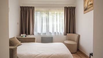 A hotel room with a bed, a chair, a radiator, and curtains.