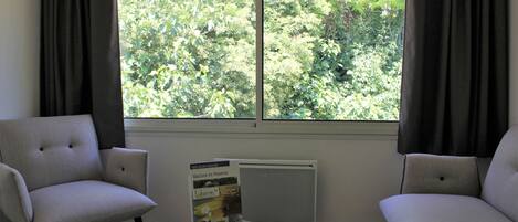 Una habitación con dos sofás, una mesita con una revista y una ventana con cortinas.
