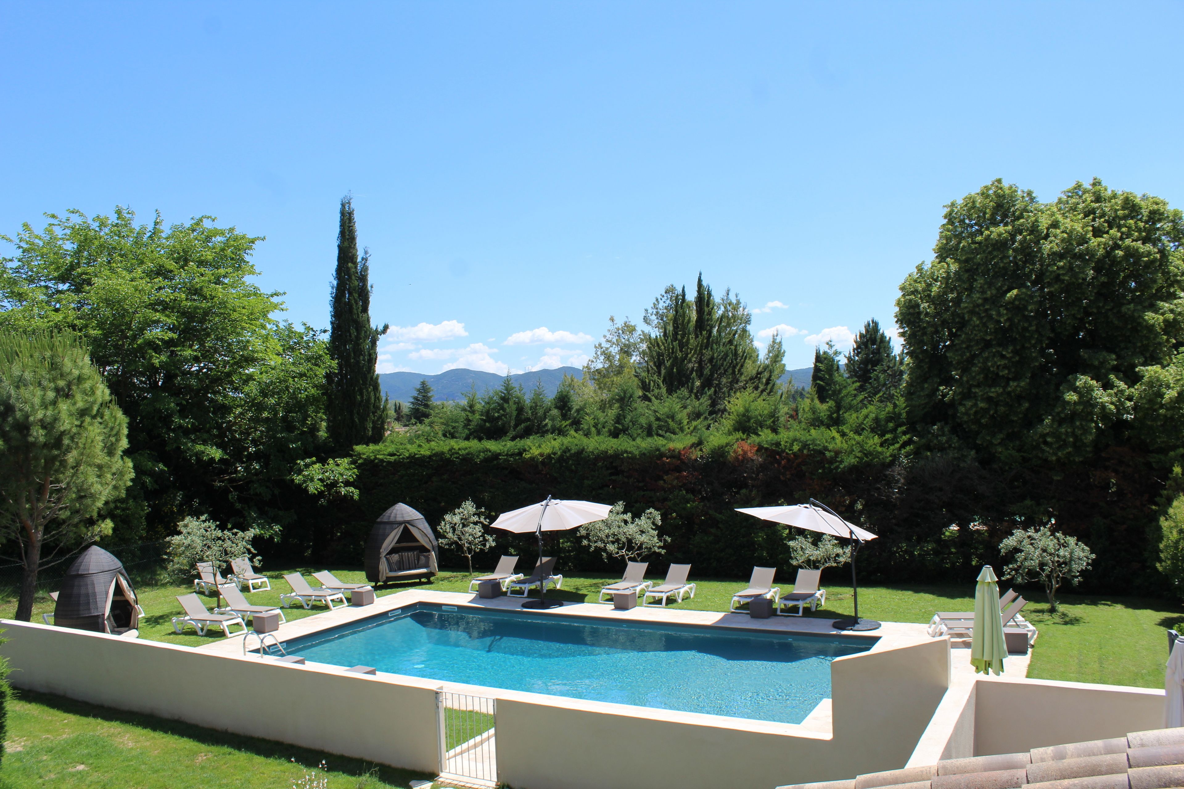A rectangular swimming pool with lounge chairs and umbrellas, surrounded by a well-maintained lawn and trees.