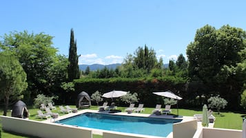 A rectangular swimming pool with lounge chairs and umbrellas, surrounded by a well-maintained lawn and trees.
