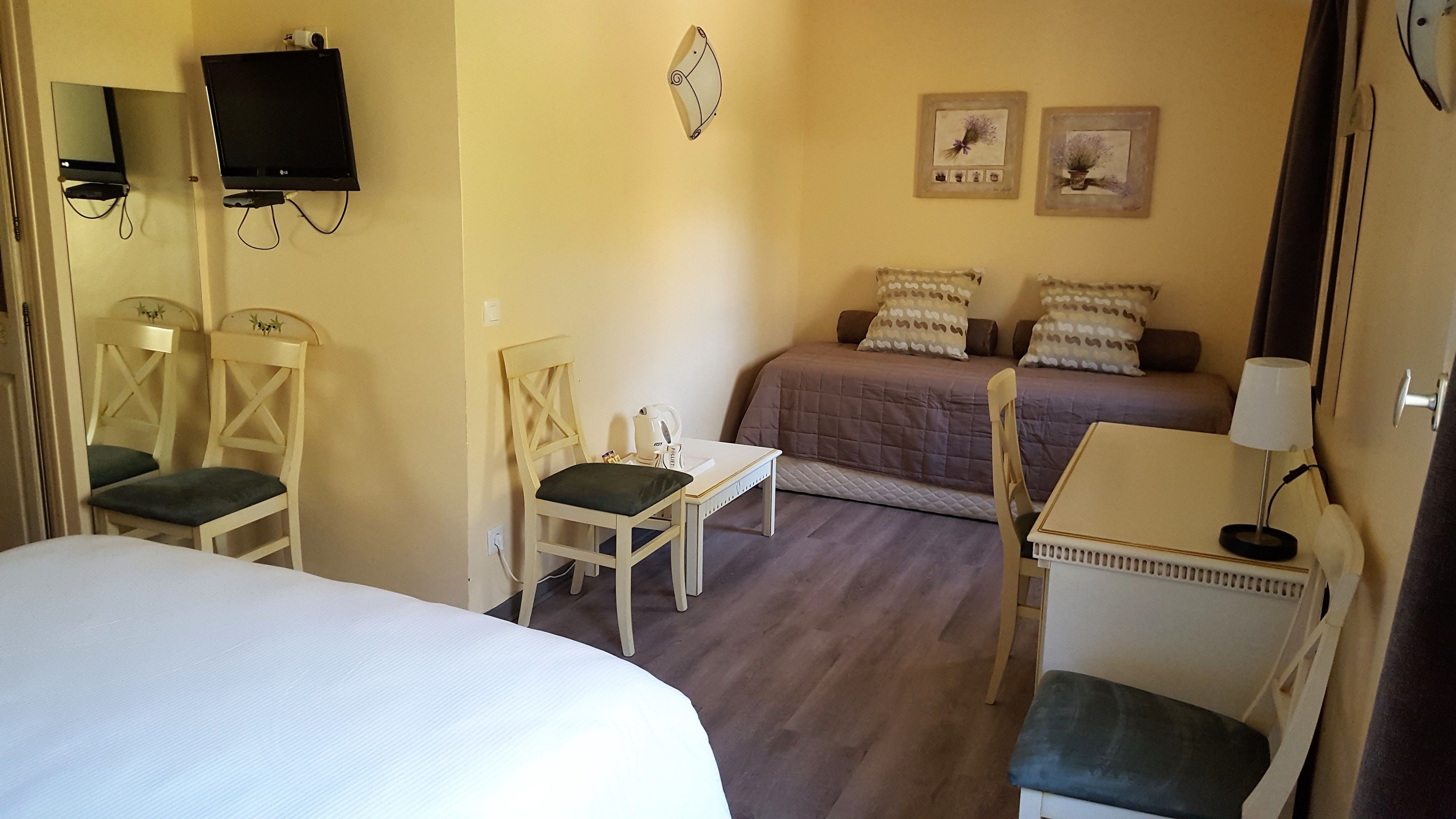 Une chambre d’hôtel avec deux lits, un bureau, une chaise, une télévision et deux tableaux encadrés au mur.